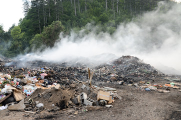 Open landfill site with burning waste. Burning pile of illegal garbage dump near city. Air and...