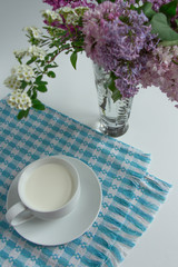 a white cup of fresh milk on a white background with sprigs of white and purple flowers that complement the composition, tasty, healthy, atmospheric