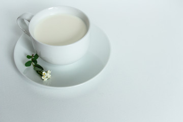 a white cup of fresh milk on a white background with sprigs of white flowers that complement the composition, tasty, healthy, atmospheric