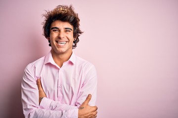 Young handsome man wearing king crown standing over isolated pink background happy face smiling with crossed arms looking at the camera. Positive person.