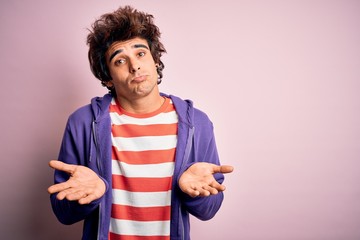 Young man wearing striped t-shirt and purple sweashirt over isolated pink background clueless and...