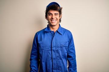 Young mechanic man wearing blue cap and uniform standing over isolated white background winking...