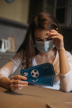 Frustrated Woman In Medical Mask Holding Sport Match Tickets At Home