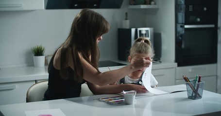 Mom and daughter paint in the kitchen. The daughter is upset and crying that she is not succeeding. Mother reassures her. Parenting concept