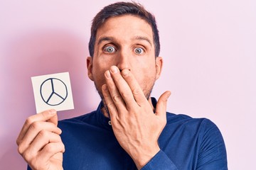 Young handsome man holding reminder with peace symbol over isolated pink background covering mouth...