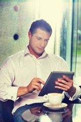 Portrait of attractive businessman using digital tablet while sitting and drinking coffee in lobby
