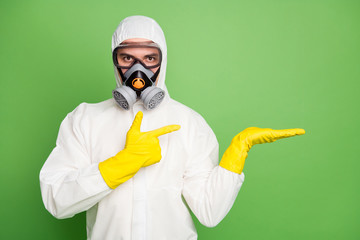 Portrait of medical worker man hold hand point index finger copyspace indicate covid19 prevention promo adverts wear latex hazmat uniform isolated over green color background