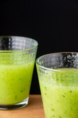 Close-up of two glasses with cucumber juice, with selective focus, on wooden box, black background, vertical, with copy space