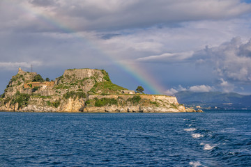 Fototapeta na wymiar View of ancient venetian fortress on the hill at Corfu Island, Greece. Old stone walls, covered with green grass, sea bay, blue sky and rainbow
