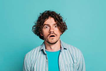 Young wondered man posing with open mouth on camera. Portrait of guy isolated over blue background. Emotional man on picture.