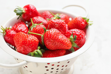 Colander with ripe strawberry on light background