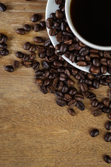 White coffee cup and coffee beans on wooden table with copyspace for text. Selective focus.