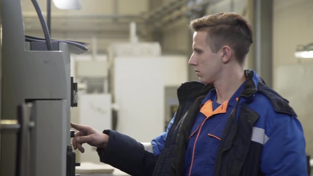 Young male operator of CNC milling machine stands at control panel in the workshop. High precision CNC machining center working, operator machining metal blank process in industrial factory