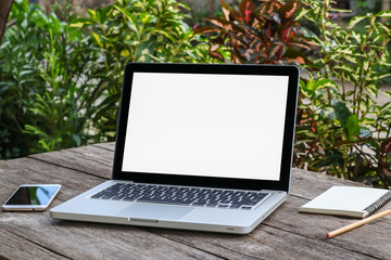 Laptop computer with white blank screen monitor with mobile and notebook on old wooden table with blurred background