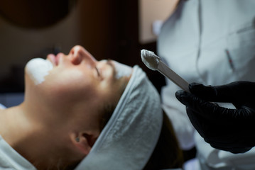A close-up photo of peeling gommage on a stick near a young woman's face on a beauty bed. A...