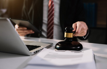 Justice and law concept.Male judge in a courtroom the gavel, working with digital tablet computer on wood table in sun light.