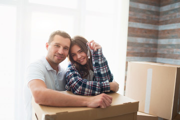 stand near cardboard boxes and look at the camera. In the hands of his wife the keys to a new housing, apartment, house.