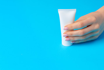 Female hand holding skincare product bottle on blue