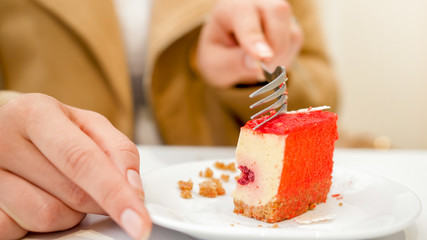 Closeup image of young woman holding fork and eating sweet red cake