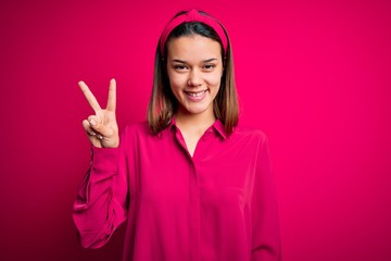 Young beautiful brunette girl wearing casual shirt standing over isolated pink background showing and pointing up with fingers number two while smiling confident and happy.