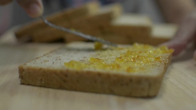 Close up people's hand spreading organic orange marmalade on sliced wholewheat bread with a knife on a wooden table. Healthy eating concept.