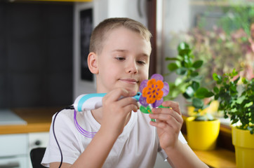 Child using 3D pen. Happy boy making flower from colored ABS plastic.