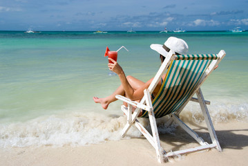 Frau im Liegestuhl mit Cocktail am Strand