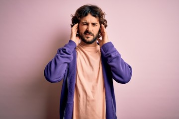 Young handsome sporty man with beard wearing casual sweatshirt over pink background covering ears...