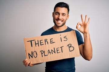 Young handsome activist man protesting for the enviroment hoding cardboard doing ok sign with fingers, excellent symbol