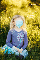 Fototapeta premium Young girl in sanitary face mask covering her face. Child wearing protective mask against coronavirus outdoors. Concept of panic, safety and health protection during covid-19 quarantine.