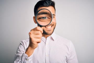 Fototapeta na wymiar Young detective man looking through magnifying glass over isolated background with a happy face standing and smiling with a confident smile showing teeth