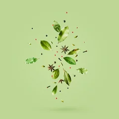 Poster Creatieve mockup met vliegende verschillende soorten kruiden Laurierblad, rode peper, anijs op groene achtergrond met kopieerruimte. © PINKASEVICH