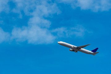 Fototapeta na wymiar Airplane is flying on blue sky background with copy space. White soft clouds and a blurry half-moon visible