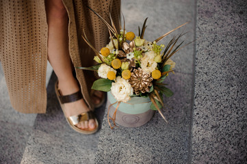 flower arrangement in box stands on the floor near woman's legs