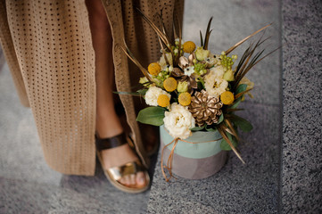 stylish flower arrangement in box stands on the floor near woman's legs