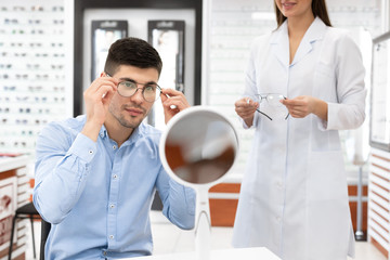 Specialist helping young guy to choose glasses