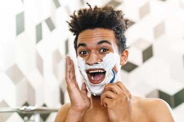 Photo of african american man shaving with foam while looking at mirror