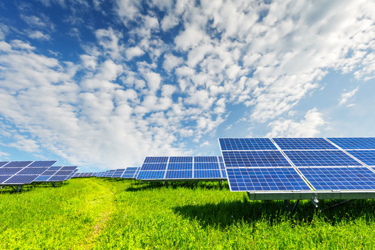 Solar panel on blue sky background. Green grass and cloudy sky. Alternative energy concept