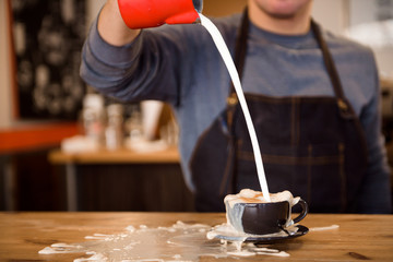 Close up barista pouring too much milk in coffee cup, making latte art