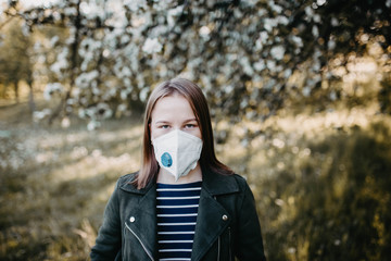 young woman in a medical mask with a valve in a summer park with flowering trees.