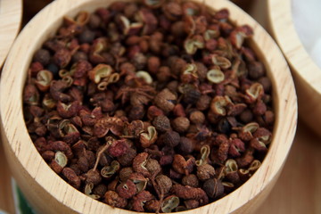 Fruits of Japanese prickly ash or Sichuan pepper in ligth brown bowl. Seed is black color and peel are cracked.