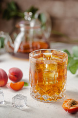 Glass of peach or apricot iced tea with fruit slices against white background