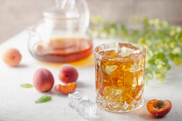 Glass of peach or apricot iced tea with fruit slices against white background