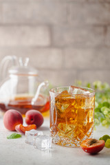 Glass of peach or apricot iced tea with fruit slices against white background