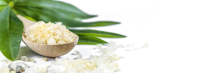 Spa banner cosmetic treatment concept. Sea resort salt, yellow solv spoon and green leaves on a white background.