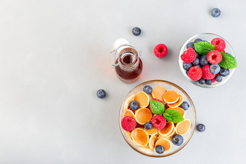 Tiny cereal pancakes served with maple syrup, raspberry and blueberry, in glass bowl, horizontal, top view, copy space