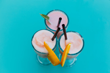 three colorful smoothie drinks on a blue table on a terrace, summer time