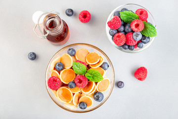 Tiny cereal pancakes served with maple syrup, raspberry and blueberry, in glass bowl, horizontal, top view