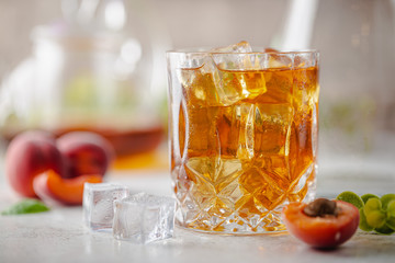 Glass of peach or apricot iced tea with fruit slices against white background