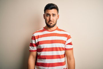 Young handsome man wearing casual striped t-shirt standing over isolated white background depressed and worry for distress, crying angry and afraid. Sad expression.